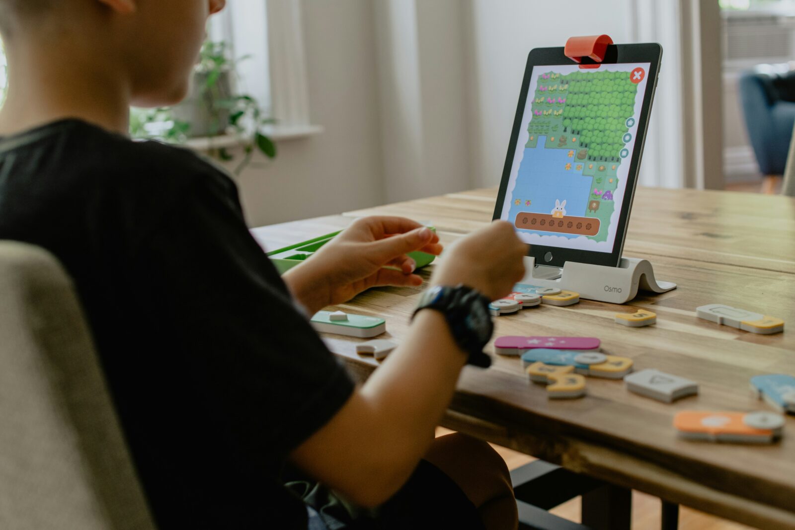 Ein Kind sitzt an einem Tisch und nutzt ein Tablet mit Lernspiel sowie interaktive Lernbausteine.