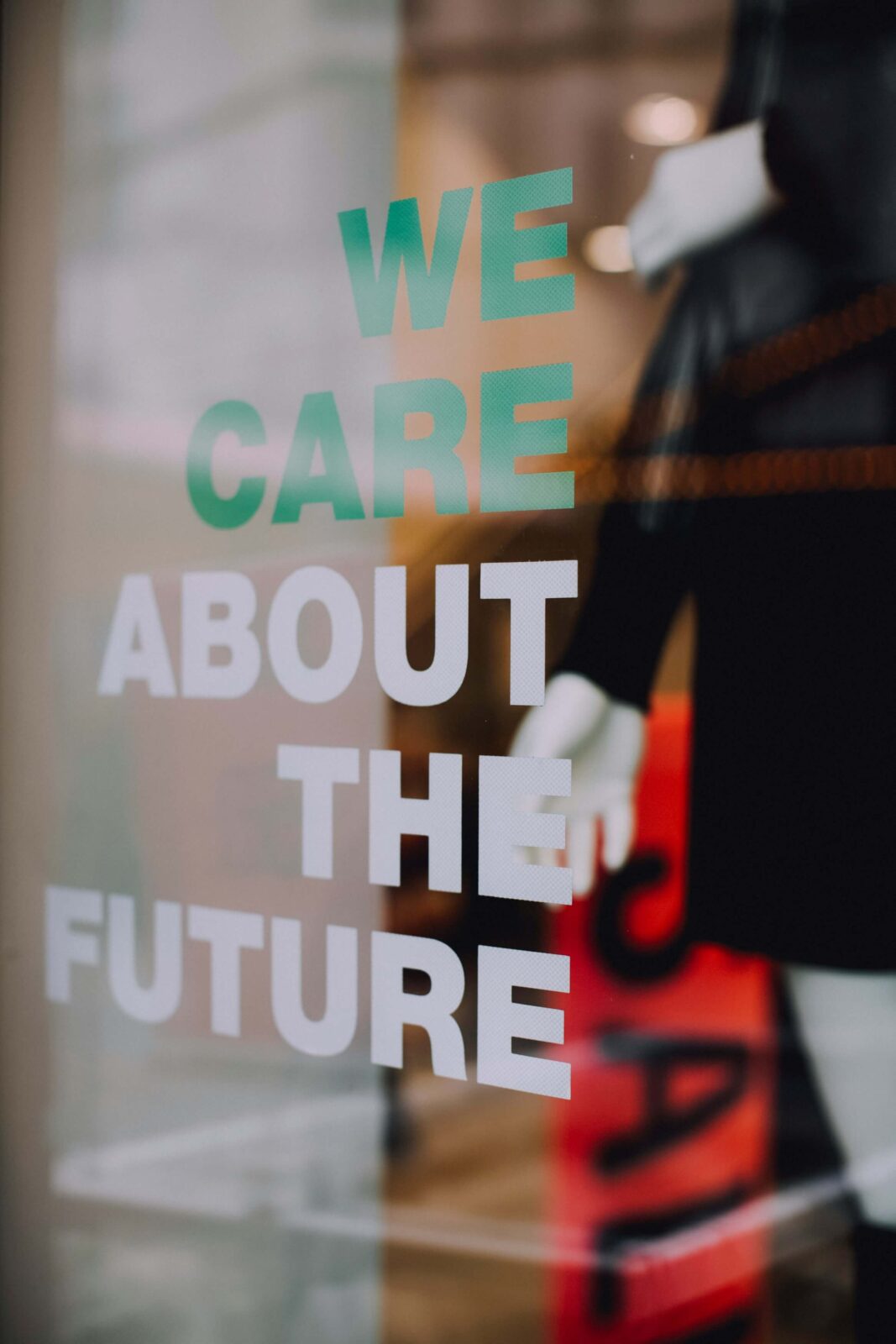 Schriftzug „We care about the future“ auf einer Glasfläche, im Hintergrund unscharf eine Schaufensterpuppe.